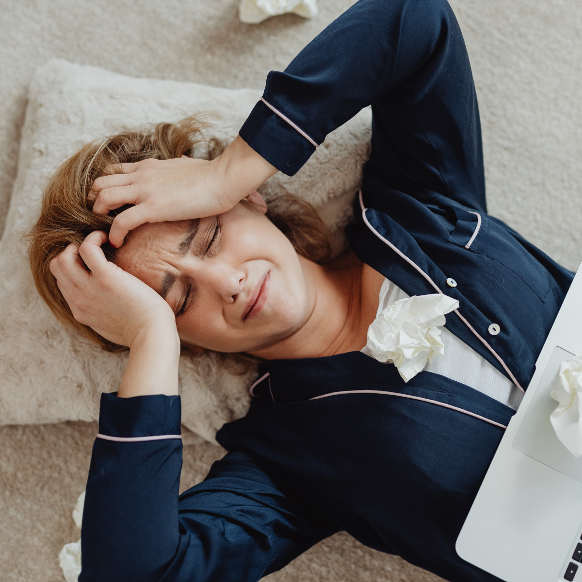 A woman lying down with her hands on her head, her expression reflecting sadness and self-doubt, symbolizing the emotional weight of impostor syndrome.