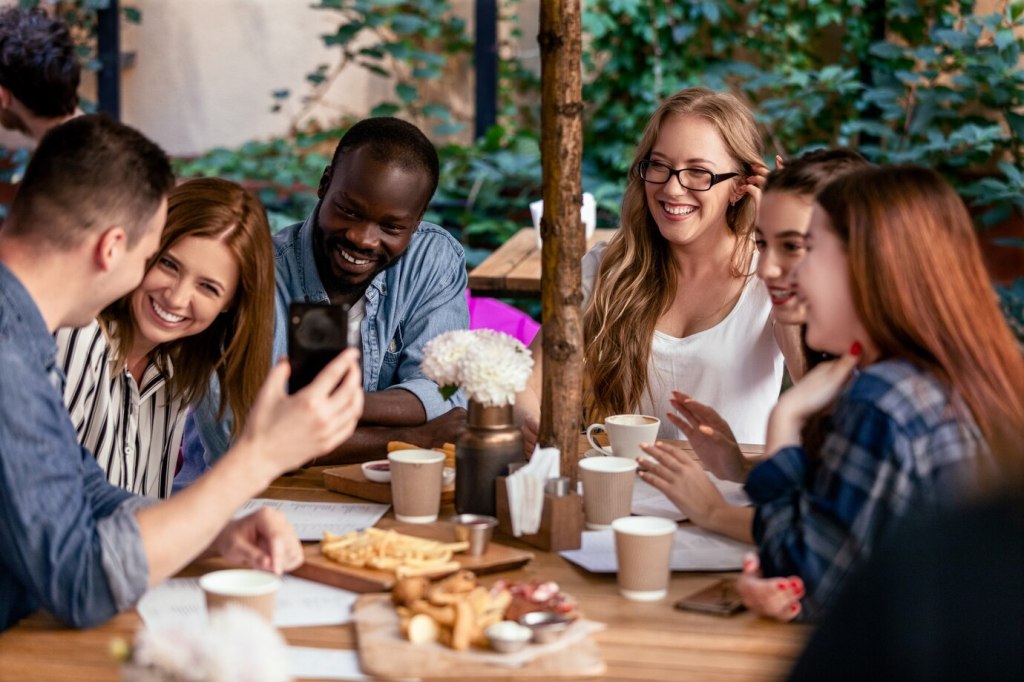 A potential employee engaging in conversation during a group lunch, networking with current or former employees. They are exchanging insights about the company culture and work environment.