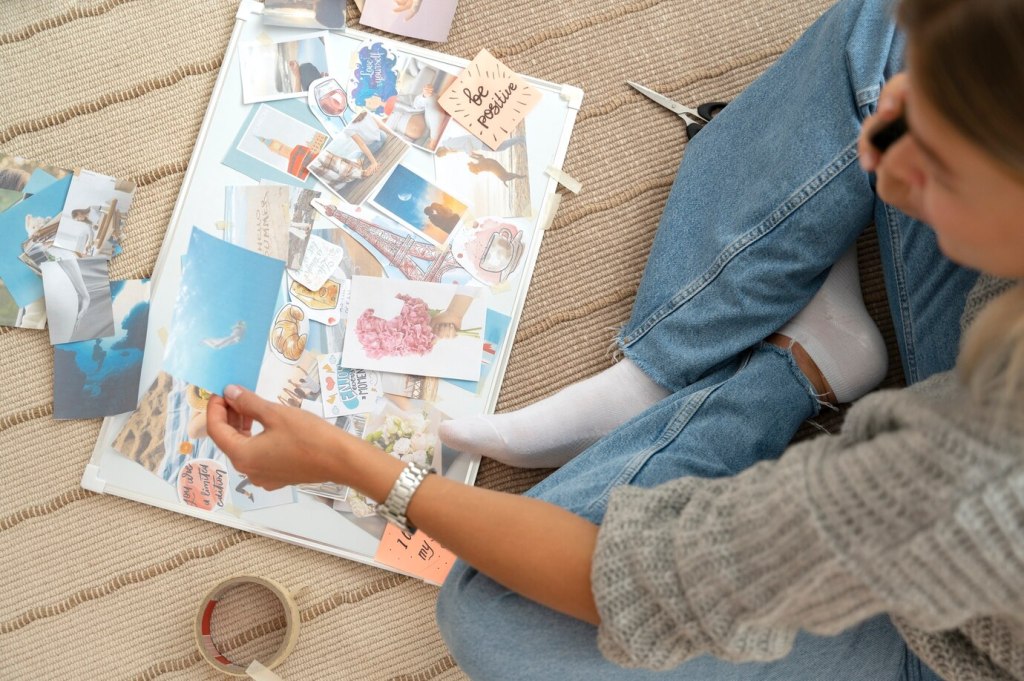 A woman sits on the floor, thoughtfully arranging papers and decorative elements in her junk journal, creating a personalized and artistic spread.