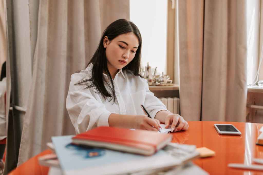 A person writing at a desk with thick, heavy drapes covering a window in the background, illustrating the use of textiles to absorb external noise and reduce echo.