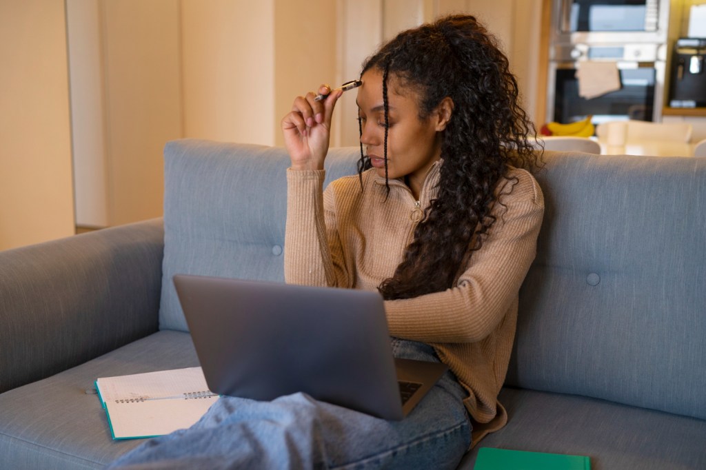 An introvert preparing for a social or professional event by doing research and planning on her laptop from the quiet comfort of her couch.