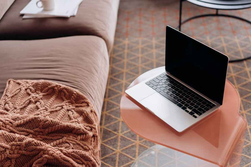 A close-up of a laptop and couch on a patterned, thick area rug, showing how floor coverings contribute mass to dampen foot traffic and ambient noise.