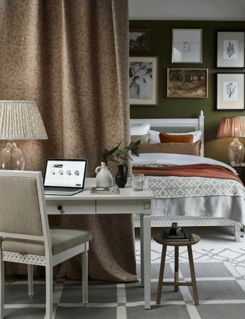 A traditionally styled room with a curtain divider separating the office and sleeping area. The space features a gray desk, complemented by classic furnishings.