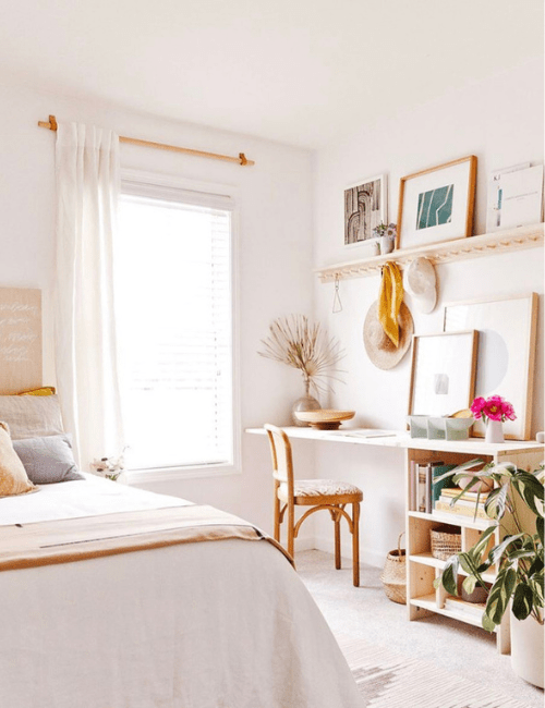 A bright room with built-in shelving, hanging plants, and a compact desk area utilizing vertical space in a bedroom office.