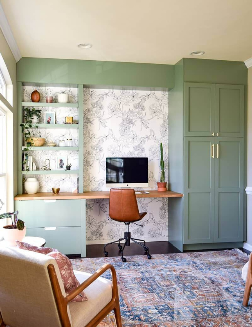 A charming space with mint green built-ins, patterned wallpaper, and a vintage-inspired desk setup.