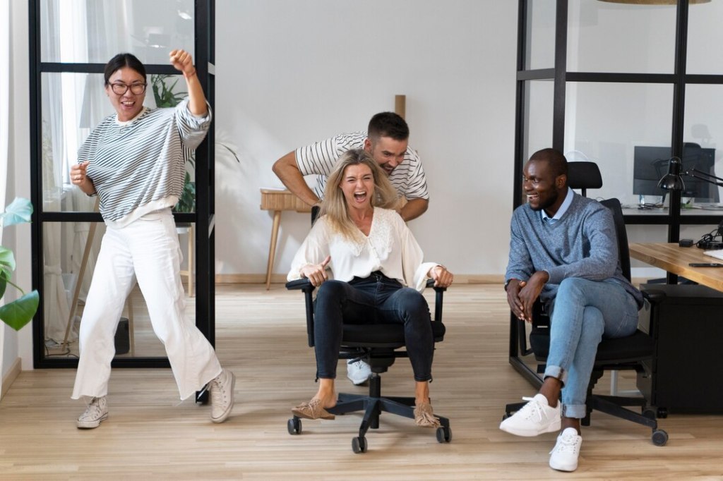 Excited coworkers having fun with office chair races in a modern workspace, showcasing how friendly competition and playful activities can create positive energy and team bonding during the workday.