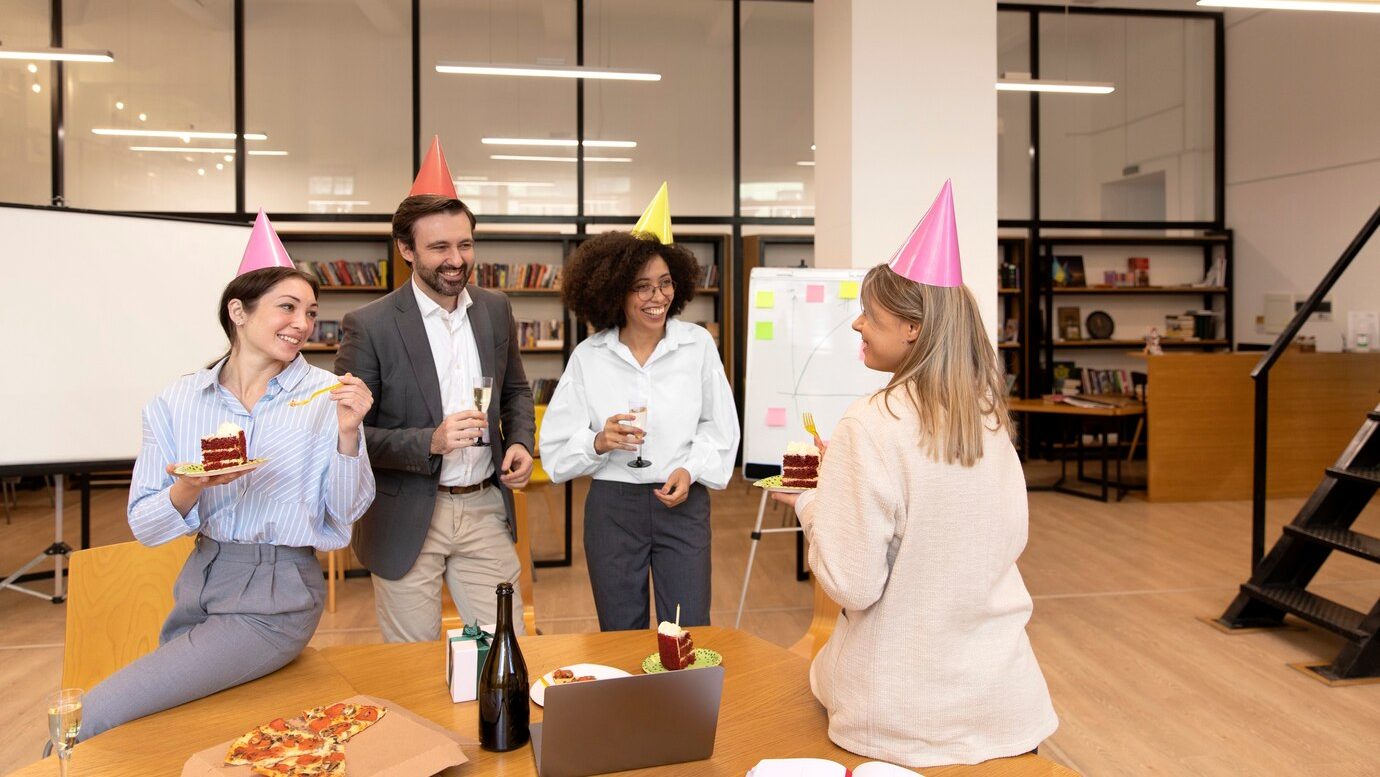 A group of coworkers gathers around, smiling and clapping as they celebrate a colleague’s birthday, reflecting a positive and supportive company culture.