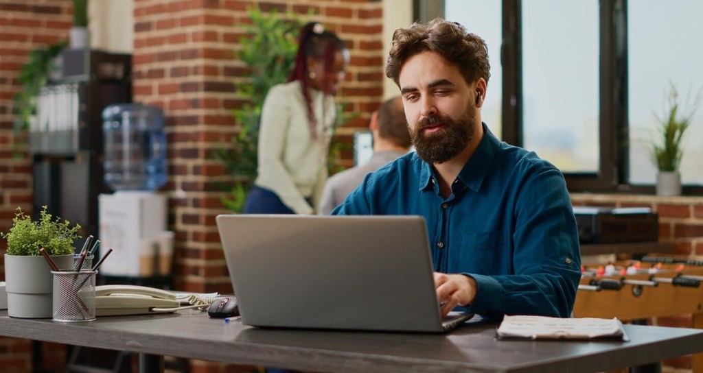 A professional male executive assistant types on his computer, efficiently managing schedules and correspondence in a modern office setting.