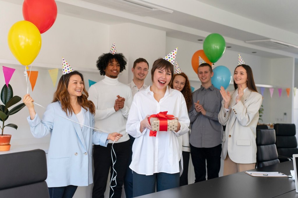 Employees celebrating a colleague's birthday with party hats and smiles, as the birthday person holds a gift. A moment of kindness and celebration in the workplace.