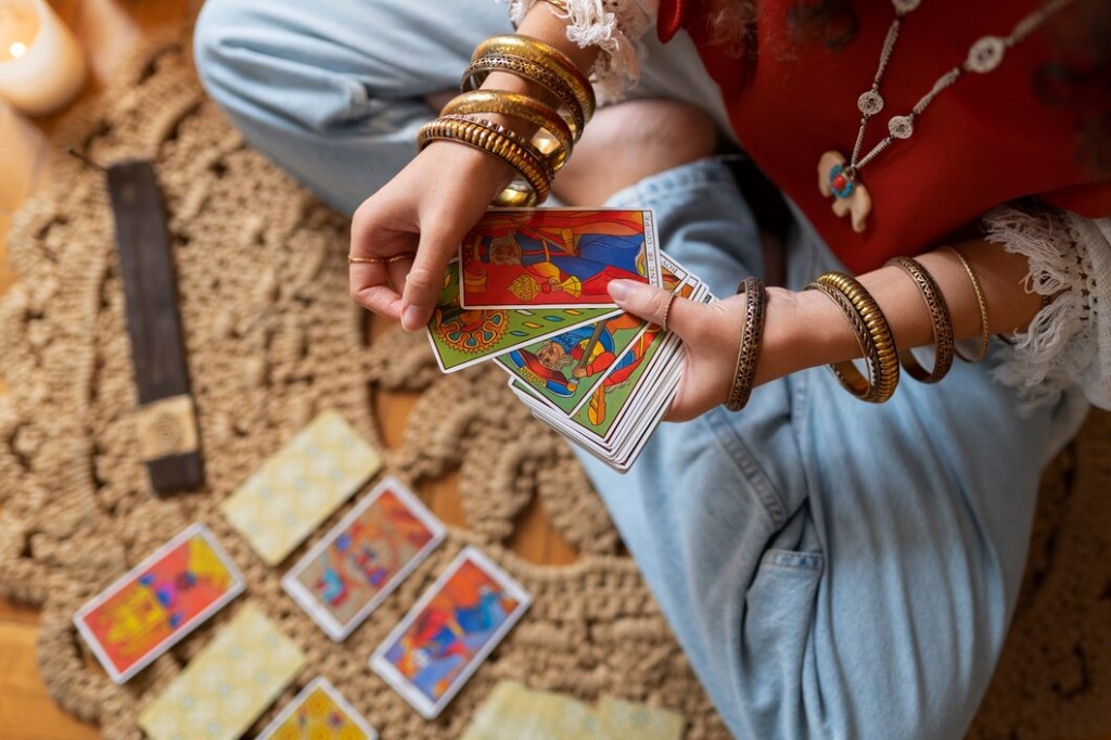 Hands adorned with golden bangles arrange colorful tarot cards on a textured rug, creating a sacred space for exploring career possibilities and uncovering professional insights.