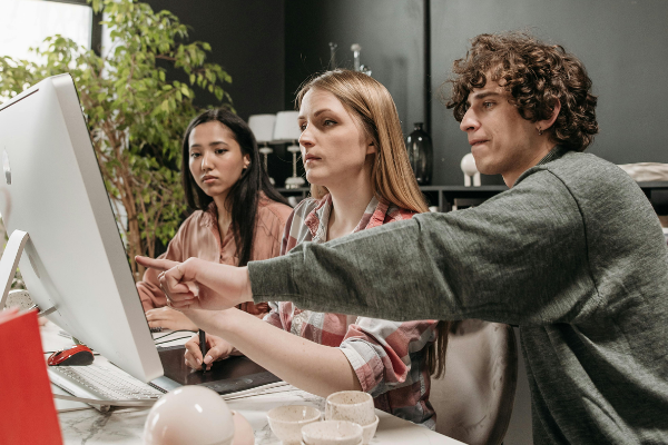 A person with a negative attitude pointing out an issue on a computer screen while collaborating with coworkers, creating a tense and unproductive atmosphere.